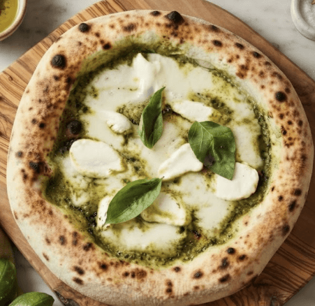 Homemade Neapolitan creamy pesto pizza with fresh basil and melted mozzarella on a wooden peel