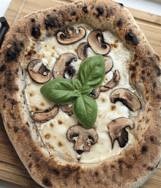 Neapolitan Pizza Bianca topped with heavy cream, mixed cheeses, mushrooms, and fresh basil leaves